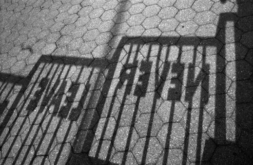 Ombre d'une rambarde dont les barreaux portent des lettres : Never Leave. New York, juin 2003.

