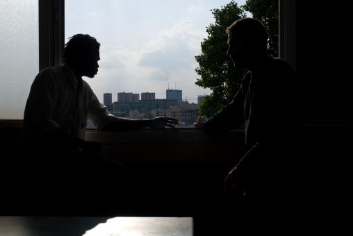 Silhouettes en contrejour de deux hommes appuyés à une fenêtre, se faisant face. Montreuil, mai 2009.
