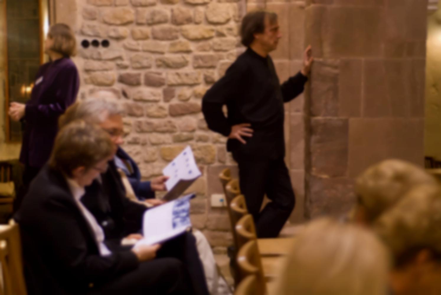 Appuyé à un pilier de l'église, le chef d'orchestre semble se concentrer, l'administratrice de l'orchestre jette un œil dans la sacristie, les premiers spectateurs lisent leurs programmes. Echternach, Luxembourg, octobre 2009.