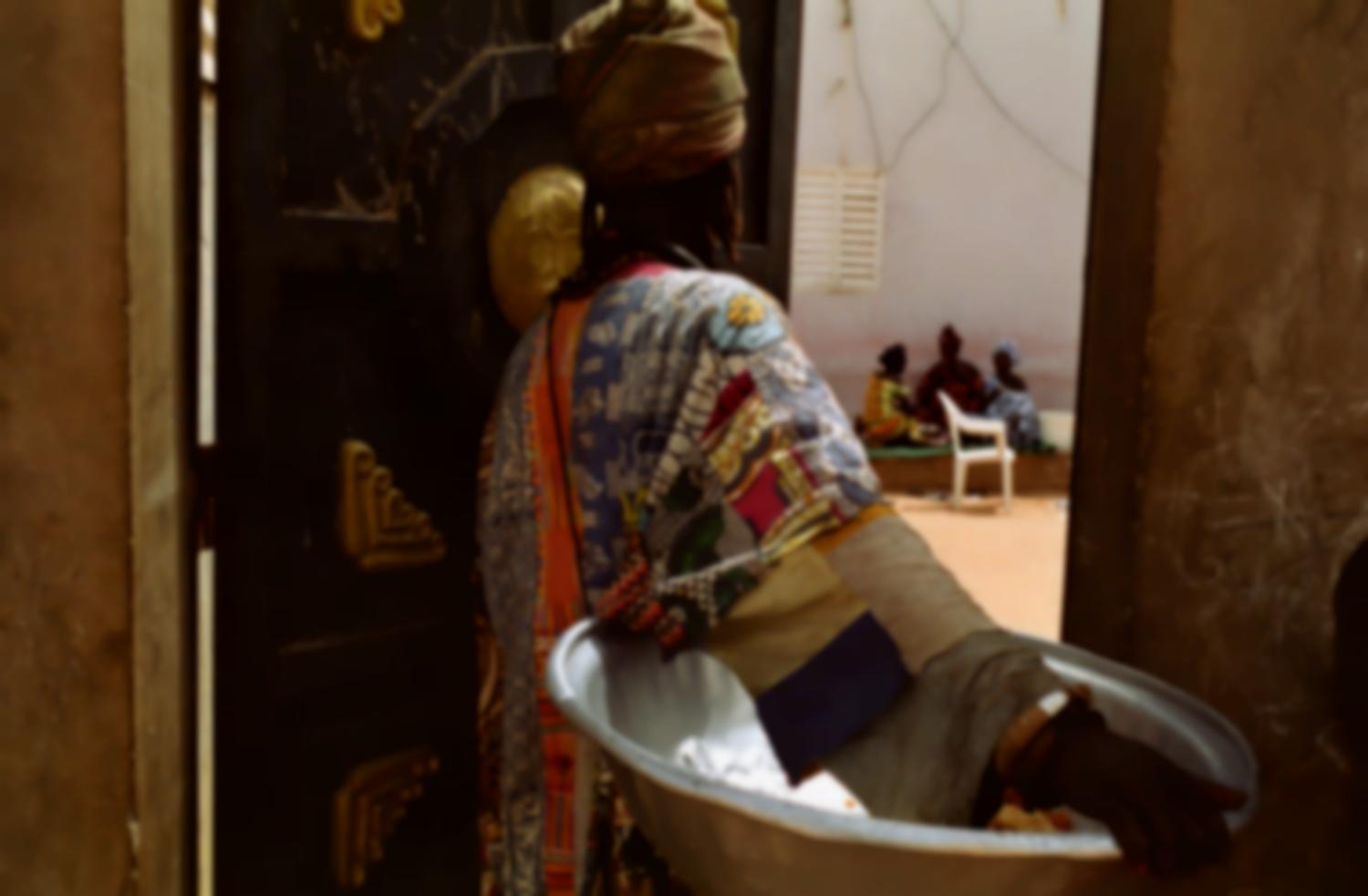 Fallou à la porte d'une concession, une grande bassine métallique sous le bras, va demander leurs restes de nourriture aux trois femmes qui se reposent dans la cour. Touba, Sénégal, février 2008.