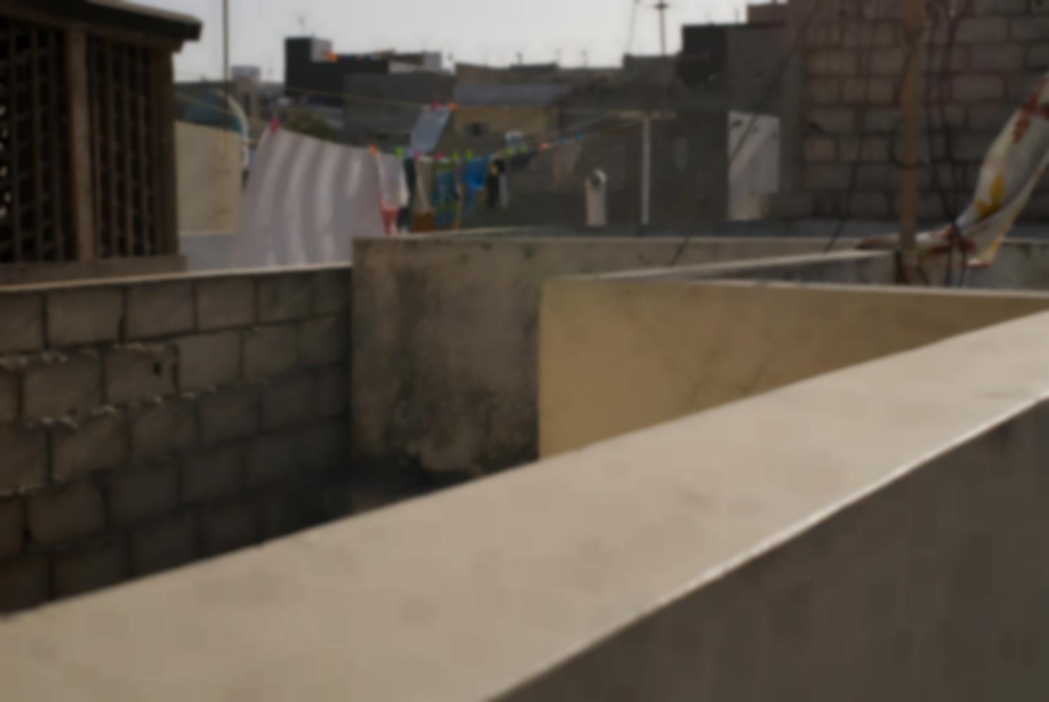 Un muret court en zigzags à angles droits devant un empilement d'édifices cubiques égayé par du linge mis à sécher. Dakar, Sénégal, mars 2010.