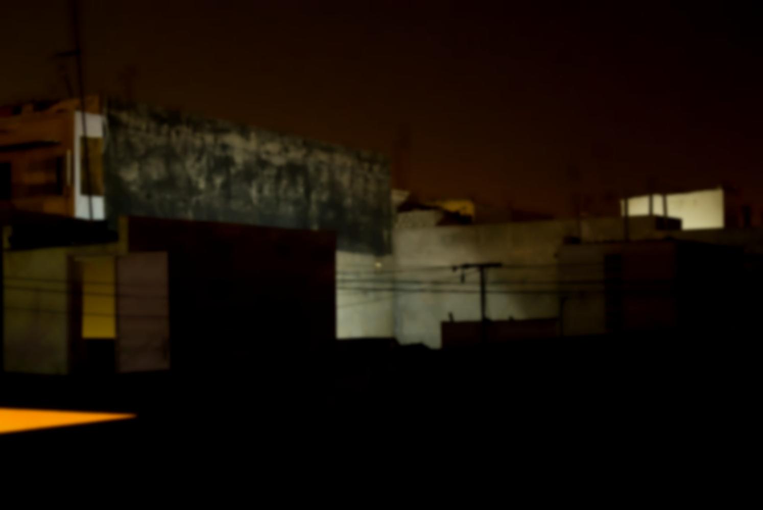Les immeubles voisins de nuit, murs de parpaings ou peints, certains éclairés par une lumière blanche, la porte d'accès à un toit voisin, des fils électriques. Dakar, Sénégal, mars 2010.