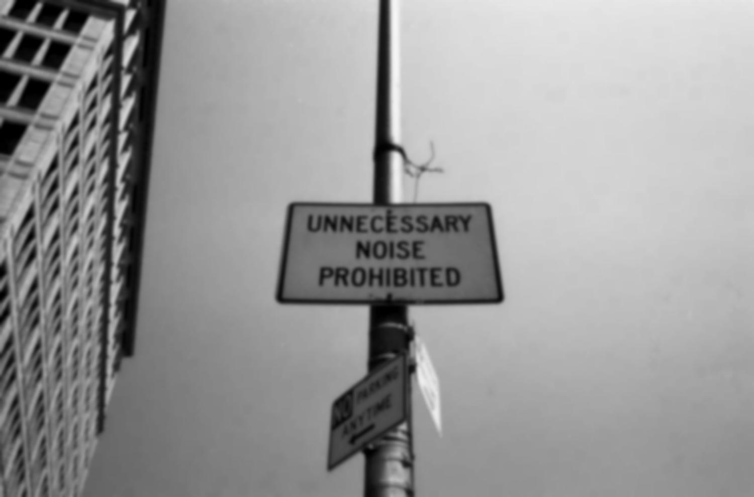 Accroché à un poteau près d'un gratte-ciel, un panneau : Unnecessary noise prohibited. New York, juin 2003.