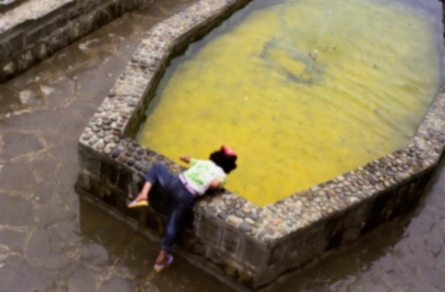 Une petite fille se penche sur un bassin au fond jaune. Masuleh, Iran, août 2006.