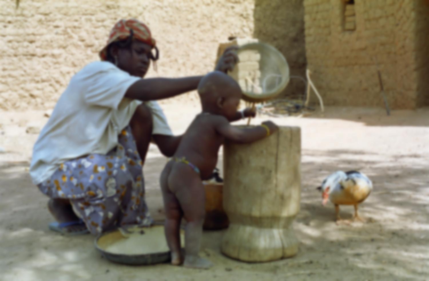 La belle-fille de Rakia verse du mil tamisé dans un mortier, sur lequel se penche son bébé. Bosseye Dogabe, Burkina Faso, mai 2008.