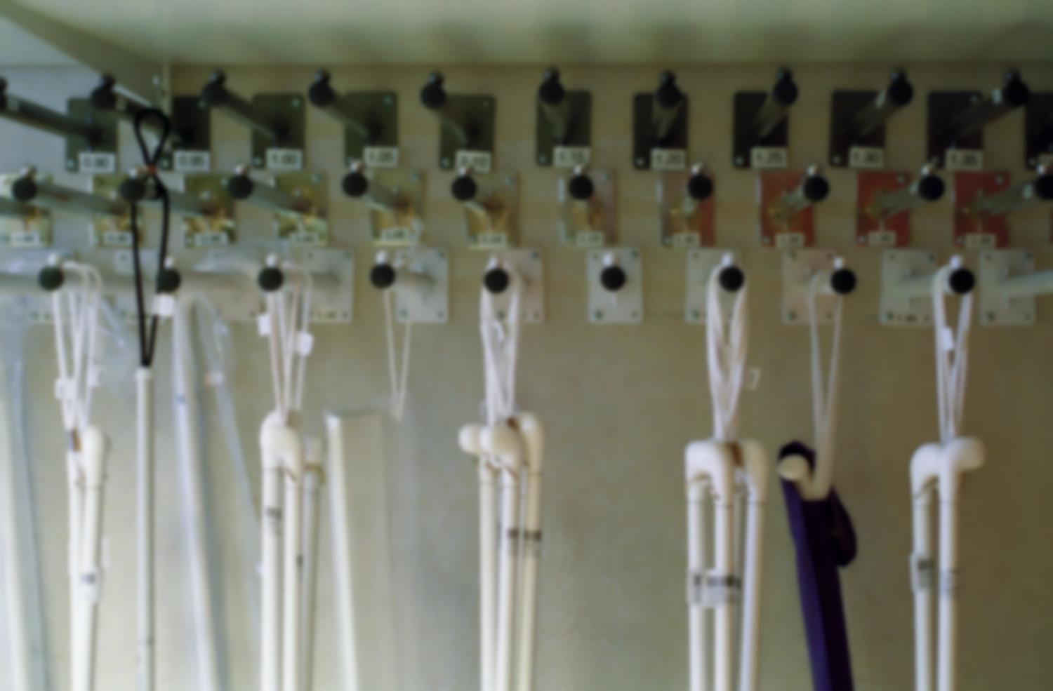 Des tiges fixées au mur sur trois rangées et étiquetées par tailles permettent de présenter les différents modèles de cannes blanches de la boutique de matériel spécialisé de l'Association Valentin Haüy. Paris, octobre 2005.