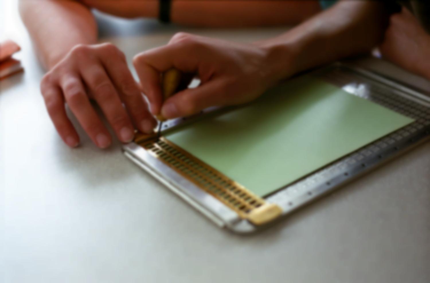 Leçon de braille à l'Association Valentin Haüy, premier essai sur une tablette pour écrire le braille : la main de l'élève guidée par celle du professeur. Paris, octobre 2005.