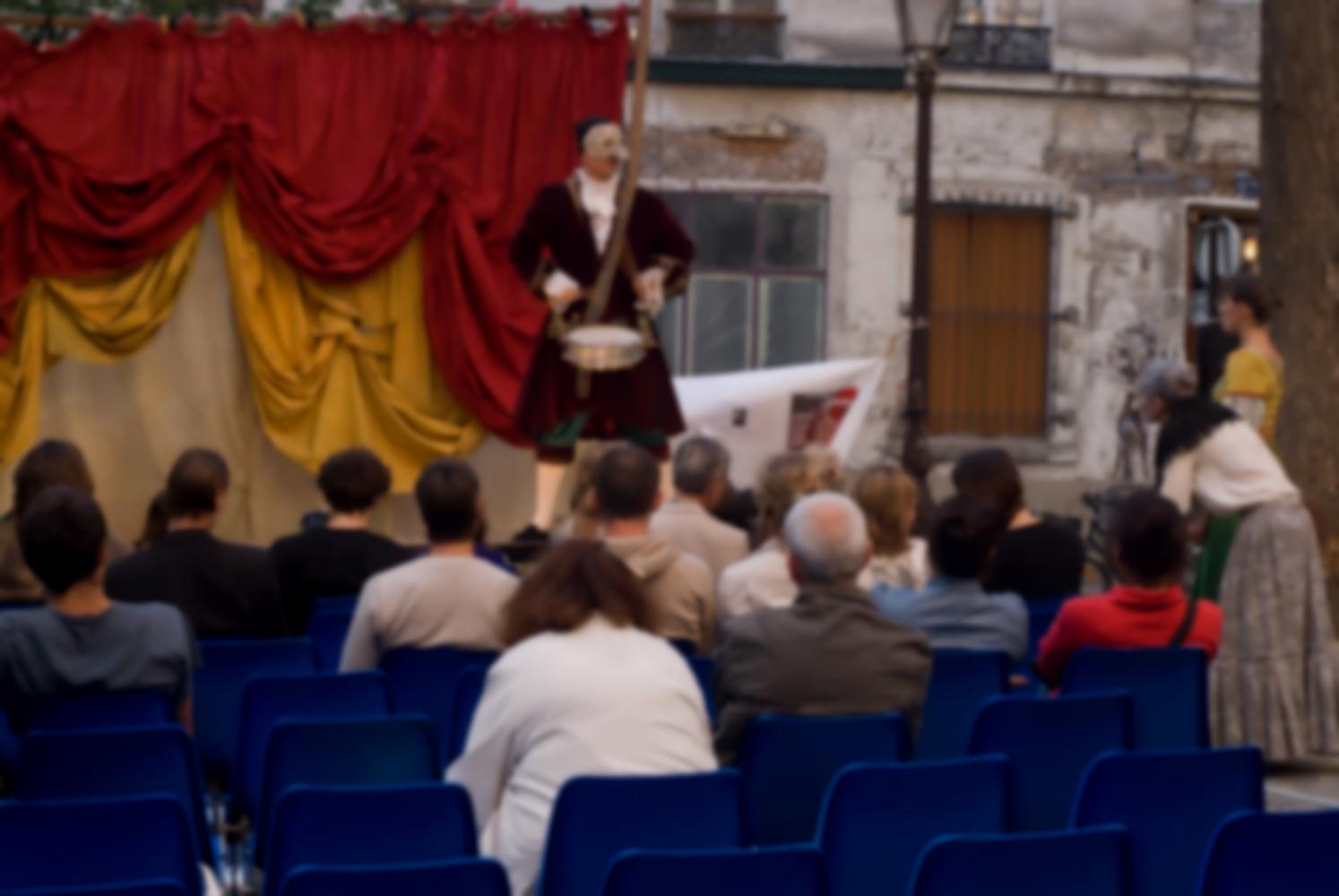 La jeune fille et la vieille femme sont passées dans le public et écoutent l'annonce d'un crieur public masqué, équipé d'un tambour. Paris, août 2010.