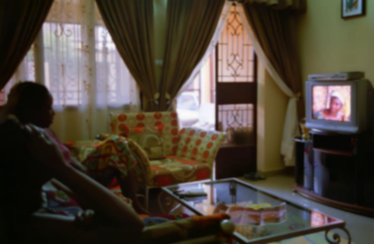 Jeanne dans son salon, assise sur le canapé près de son amie Laure, regarde la vidéo d'une série dans laquelle elles ont joué toutes les deux. Ouagadougou, Burkina Faso, juin 2008.
