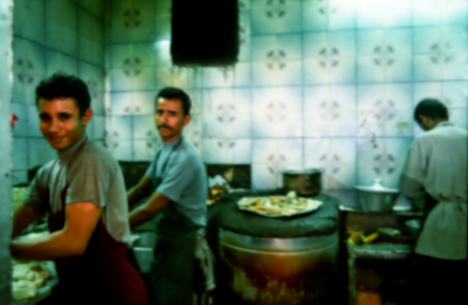 Dans la cuisine d'un restaurant aux murs carrelés de vert, deux hommes en tabliers travaillent de la pâte à pain. Sanaa, Yémen, janvier 2005.
