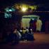 Devant la maison du marabout, sous un arbre, éclairé par une ampoule et une guirlande lumineuse, un groupe de pèlerins assis en cercle, tandis que d'autres invités entrent dans la concession. Touba, Sénégal, février 2008.