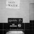 Dans les toilettes d'un restaurant, au-dessus des classiques interdiction de fumer et Employees Must Wash Hands Before Returning to Work, une feuille de papier collée sur le carrelage ordonne : SAVE WATER. New York, juin 2003.