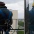 Deux ouvriers en harnais assis sur la rambarde de mon balcon, le reflet de l'un dans la fenêtre ouverte cache la silhouette de l'autre. Paris, mai 2010.
