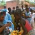 Sous les regards d'un groupe de curieux, pour la plupart des enfants, dont certains portent sur leurs têtes les marchandises qu'ils vendent dans la rue, Jeanne d'Arc achète des mangues à une petite ambulante. Ouagadougou, Burkina Faso, juin 2008.