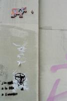 Sur un mur gris taggé, graffiti au pochoir noir représentant un visage stylisé, et plus haut, une petite vache colorée, en relief. Paris, mai 2006.