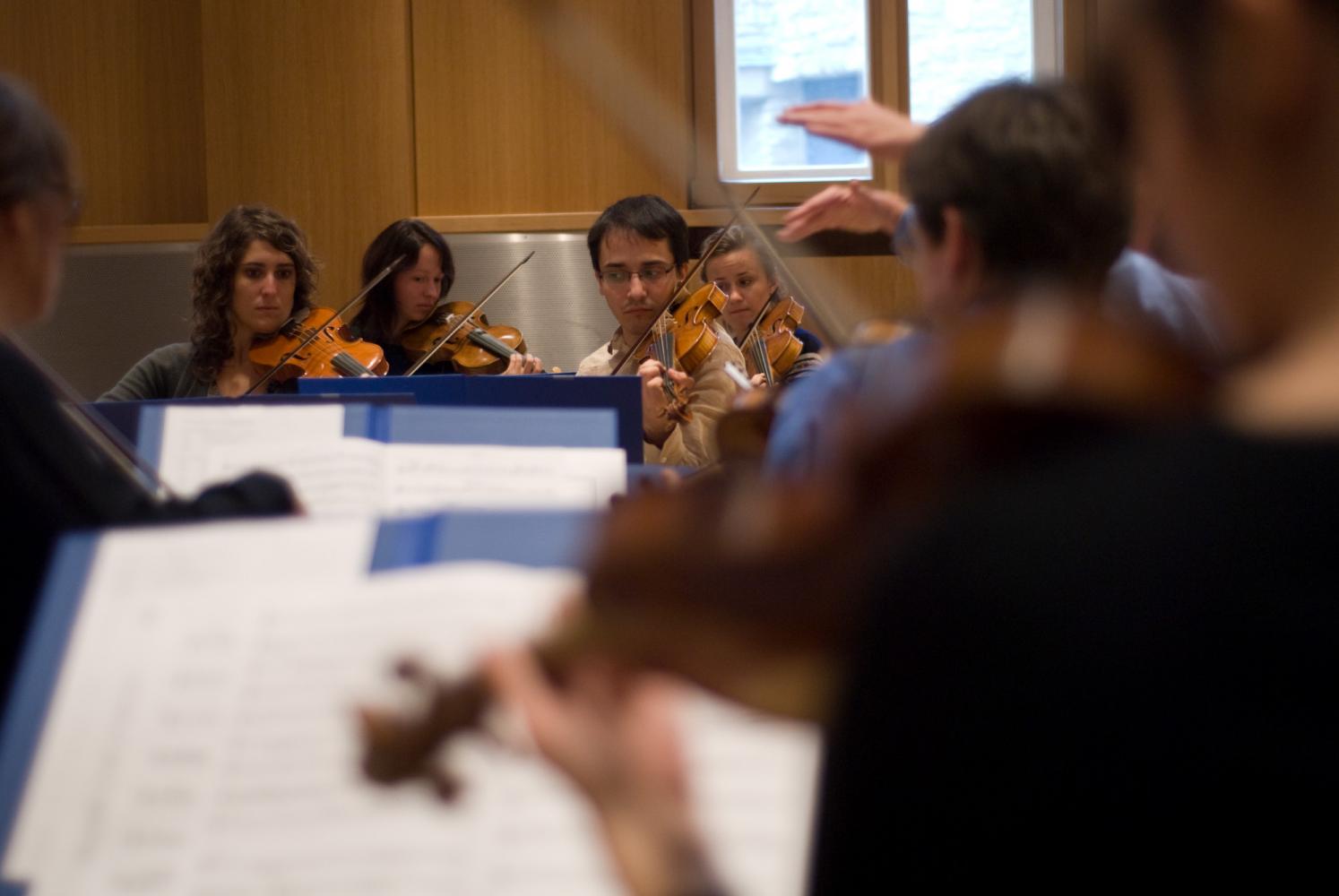 Les mains du chef d'orchestre apparaissent parmi les premiers violons, de dos au premier plan, et les seconds violons de face. Echternach, Luxembourg, octobre 2009.