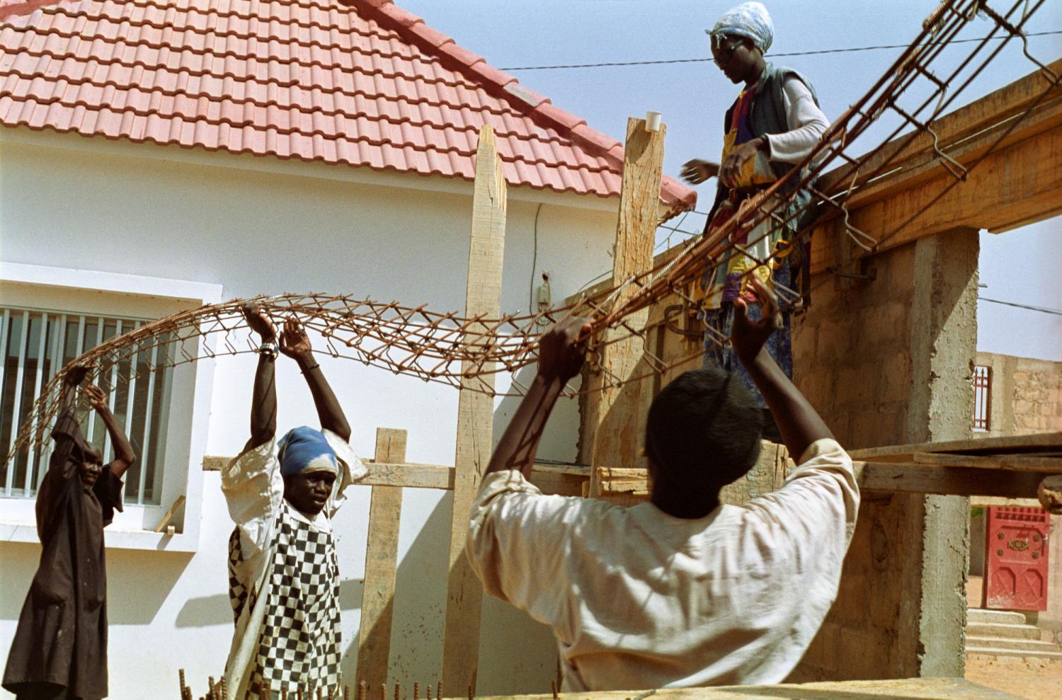 Trois Baye Fall portent une longue pièce métallique pour la passer à un quatrième perché sur l'échafaudage. Touba, Sénégal, février 2008.