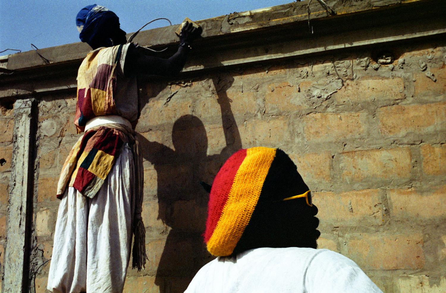 Modou prend une pause pendant que derrière lui Yapsa lisse le haut d'un mur. Touba, Sénégal, février 2008.