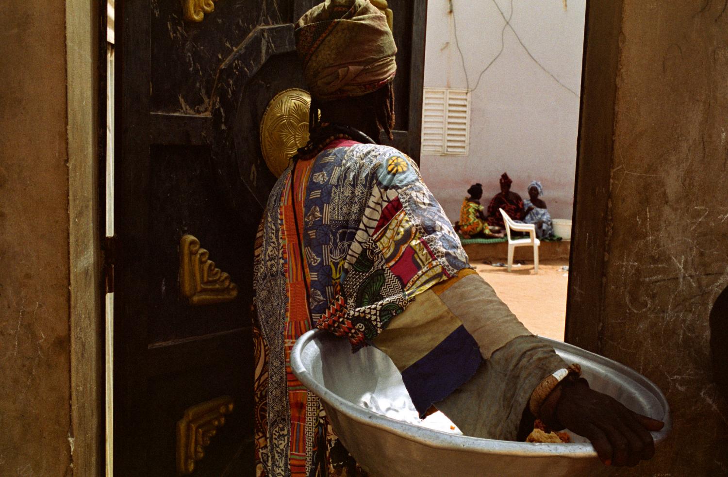 Fallou à la porte d'une concession, une grande bassine métallique sous le bras, va demander leurs restes de nourriture aux trois femmes qui se reposent dans la cour. Touba, Sénégal, février 2008.