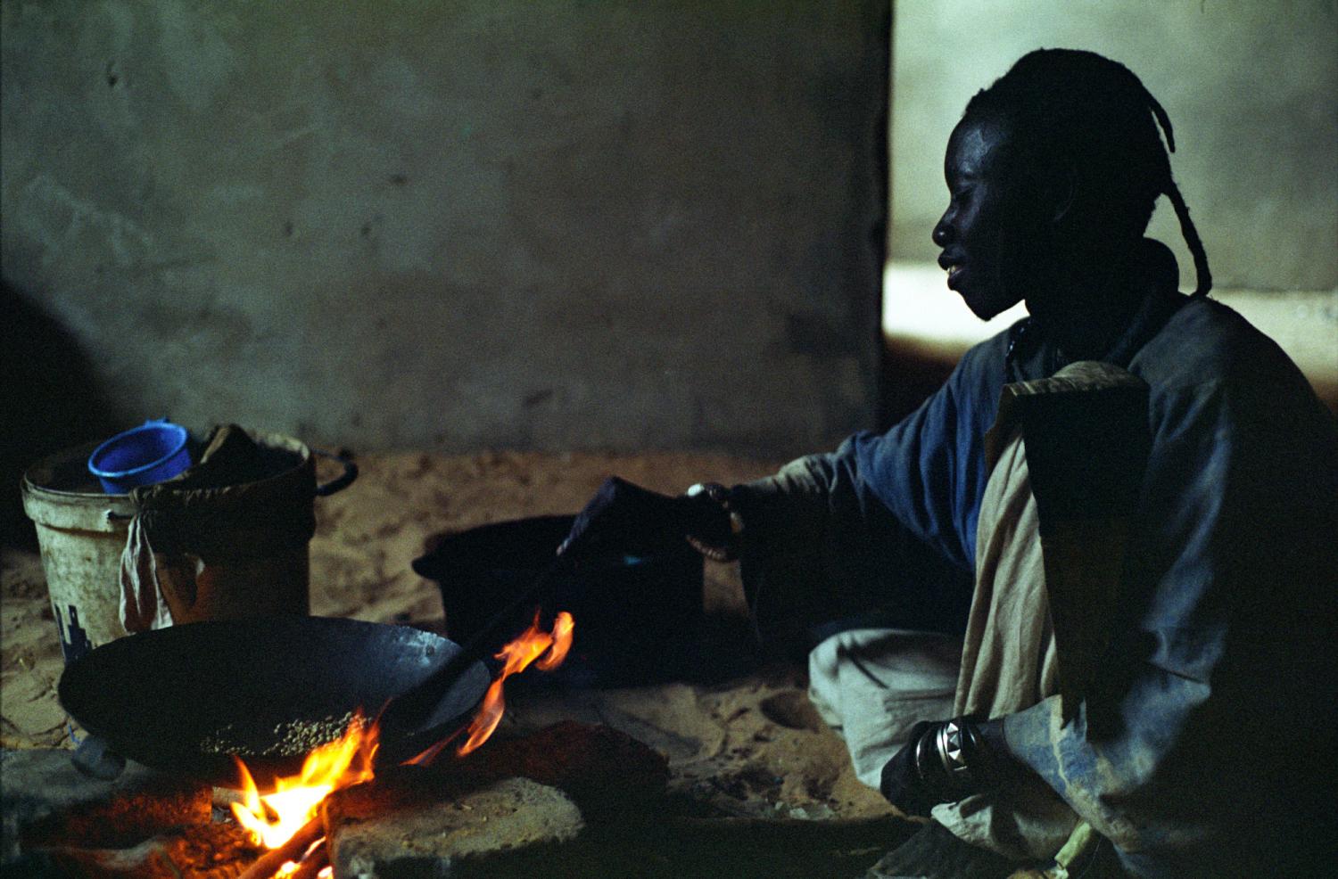 Assis devant un feu, Fallou fait griller des grains de café. Touba, Sénégal, février 2008.