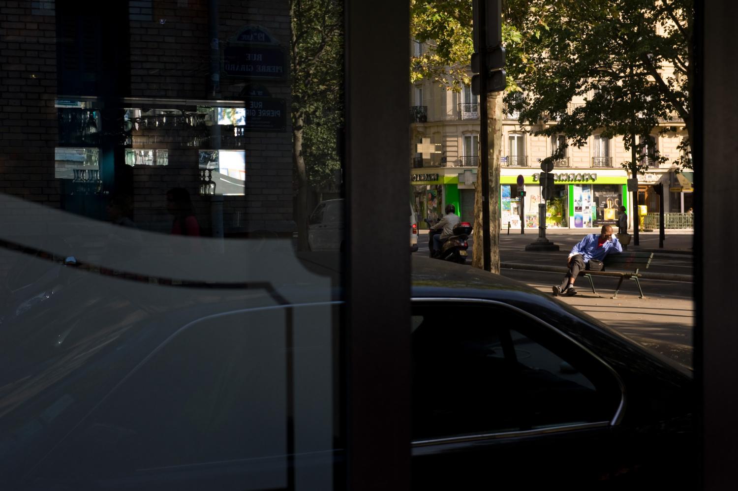 Reflet dans la devanture d'un restaurant : un homme assis sur le banc devant une des bouches de métro Laumière. Paris, juillet 2011.