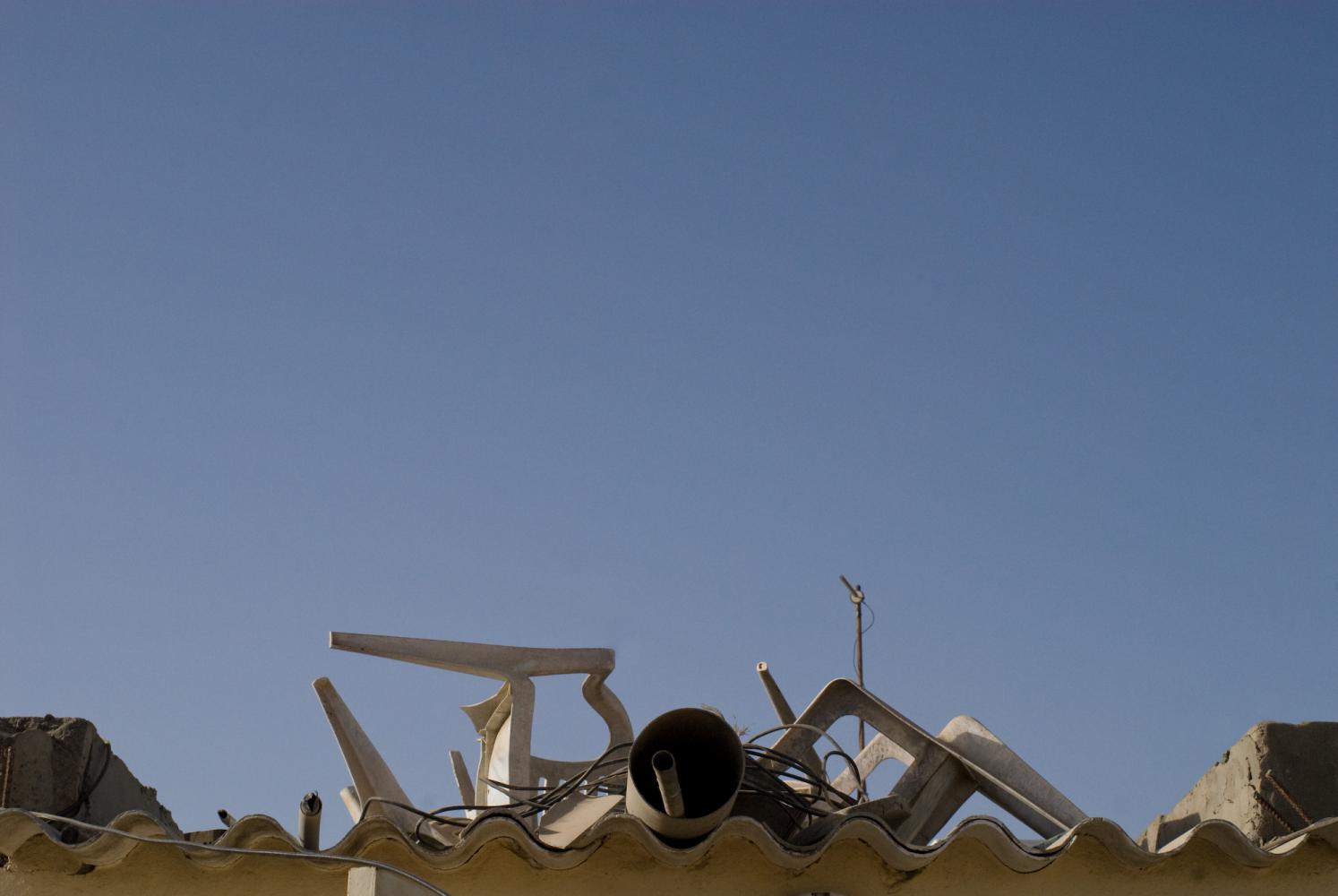 Des chaises en plastique blanc, un gros tuyau, un câble... sont empilés sur un toit de plastique ondulé, pris entre deux immeubles de parpaings. Dakar, Sénégal, mars 2010.