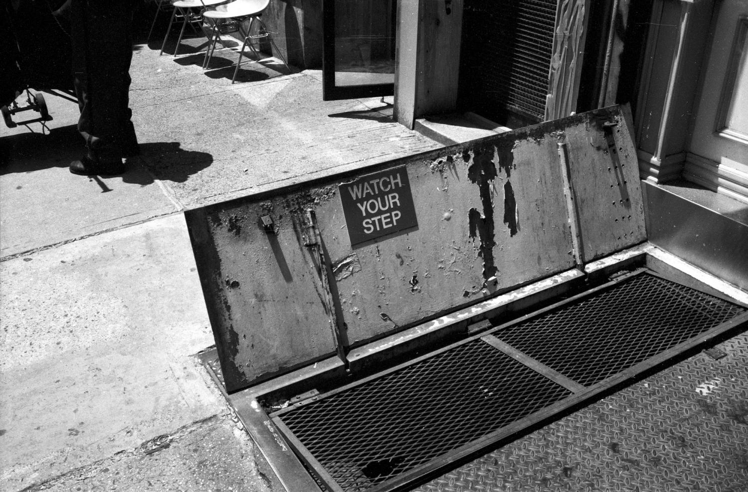 Une porte ouverte dans un trottoir donne accès à un cellier et prévient : Watch your step. New York, juin 2003.