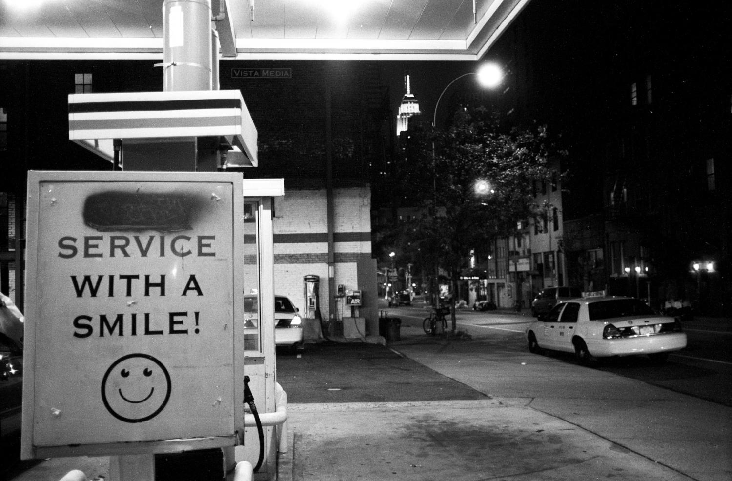 A l'entrée d'une station-service à Manhattan, sur fond d'Empire State Building, un panneau Service with a smile ! :) accueille les clients. New York, juin 2003.