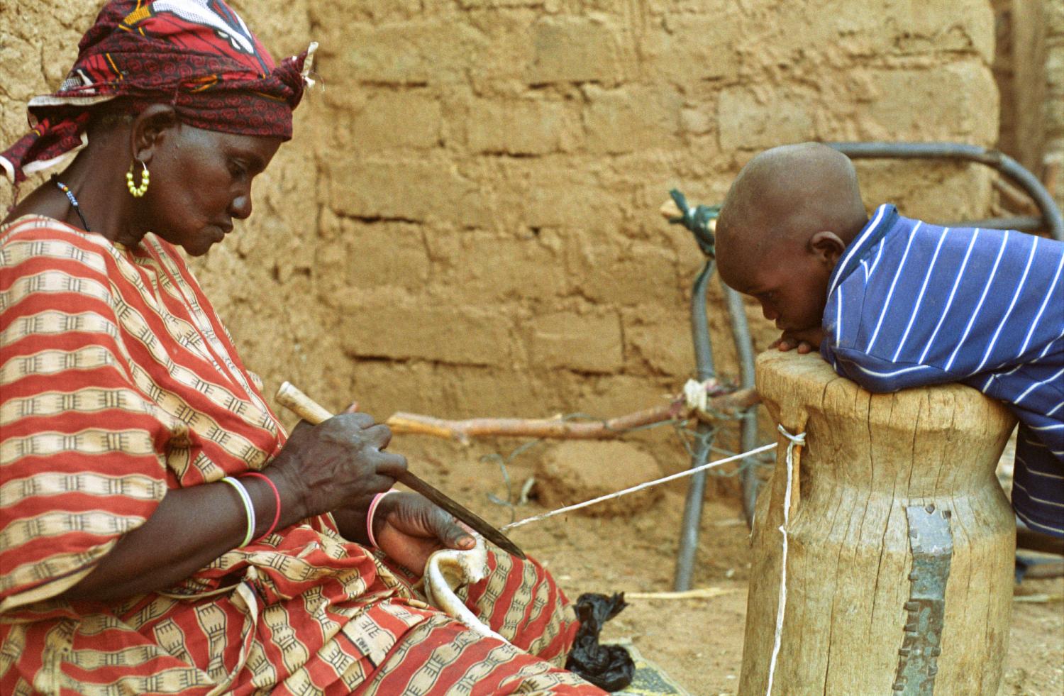 Rakia découpe une lanière de peau sous le regard attentif de son petit-fils appuyé sur un mortier renversé. Bosseye Dogabe, Burkina Faso, mai 2008.