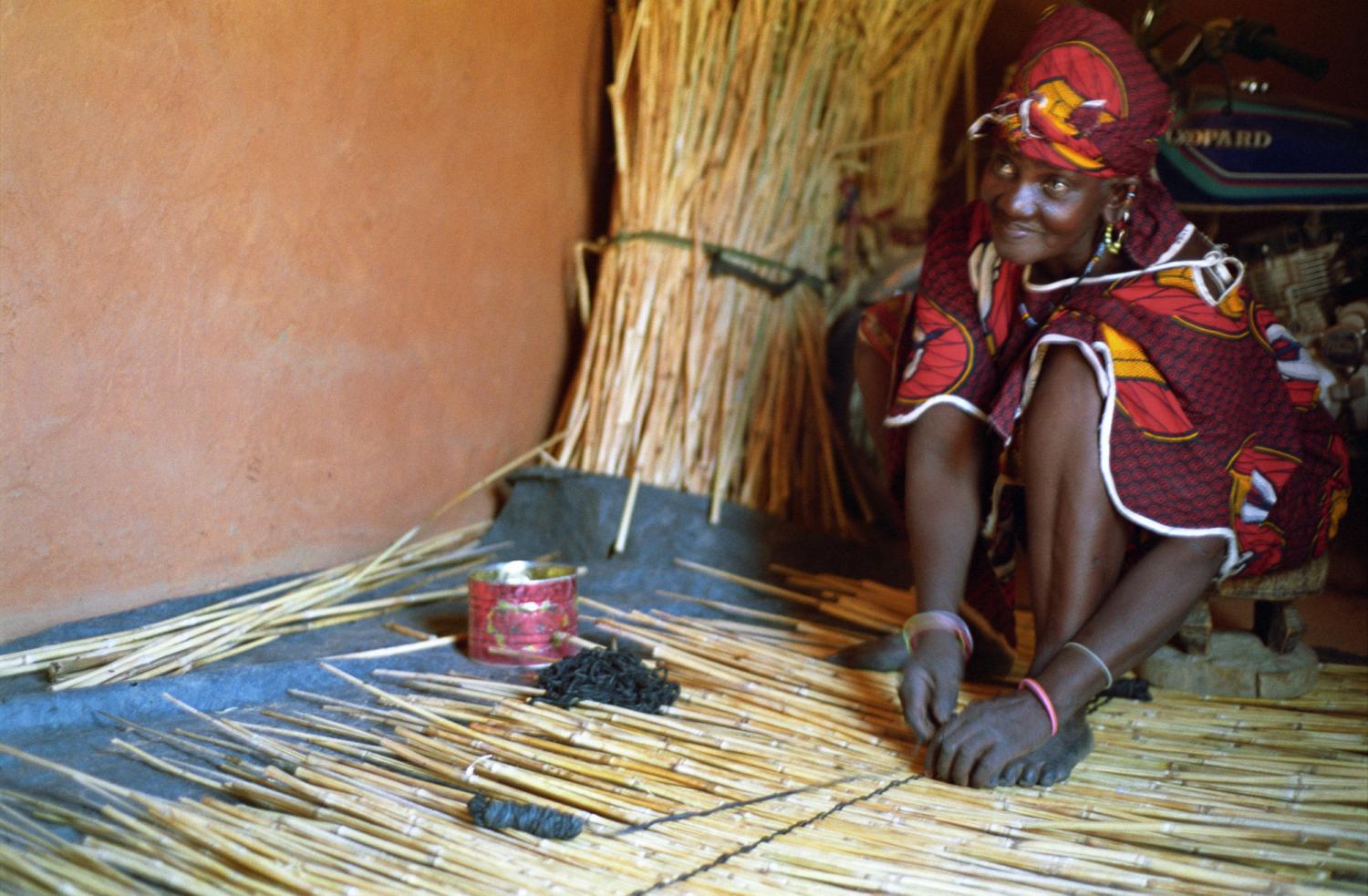 Assise sur son petit tabouret de bois, entourée de bottes de cannes de mil, Rakia finit d'ajouter le premier lien de cuir d'une nouvelle natte. Bosseye Dogabe, Burkina Faso, mai 2008.