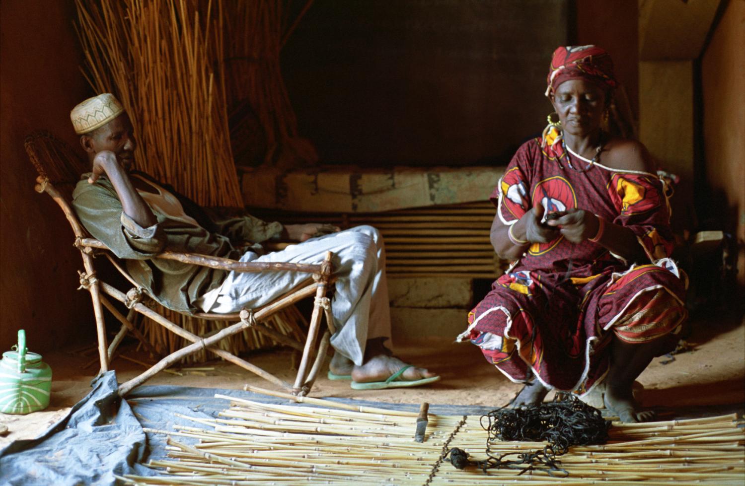 Rakia à l'ouvrage en compagnie de son ami Mohammed, assis dans un fauteuil de bois. Bosseye Dogabe, Burkina Faso, mai 2008.