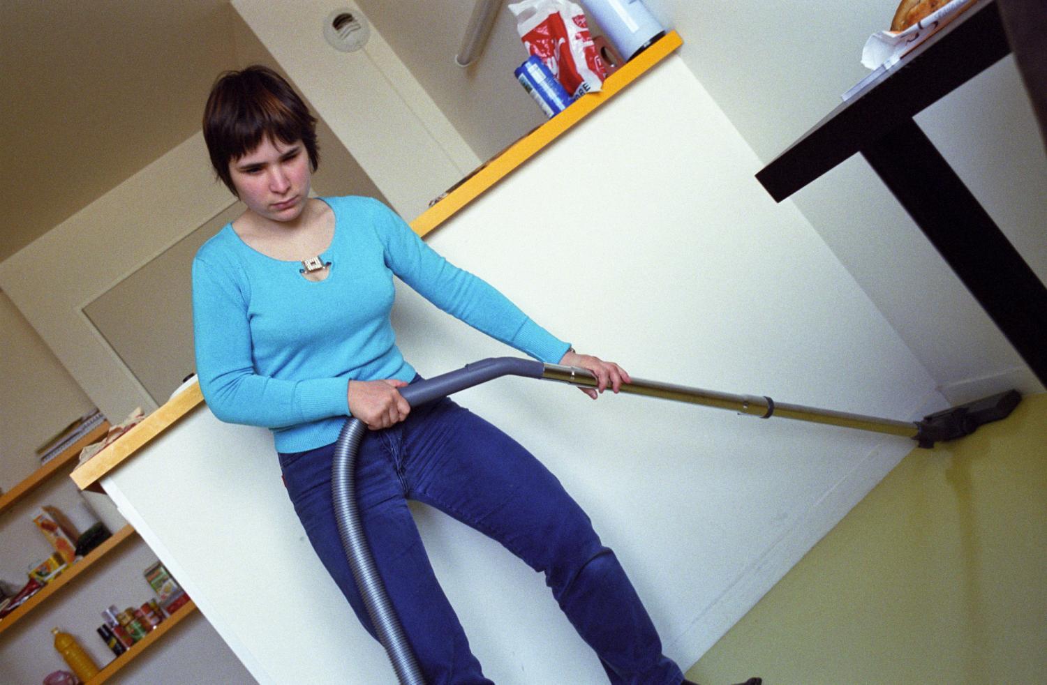 Audrey passe l'aspirateur dans sa chambre de cité universitaire sans regarder dans la direction qu'elle nettoie. Paris, avril 2006.