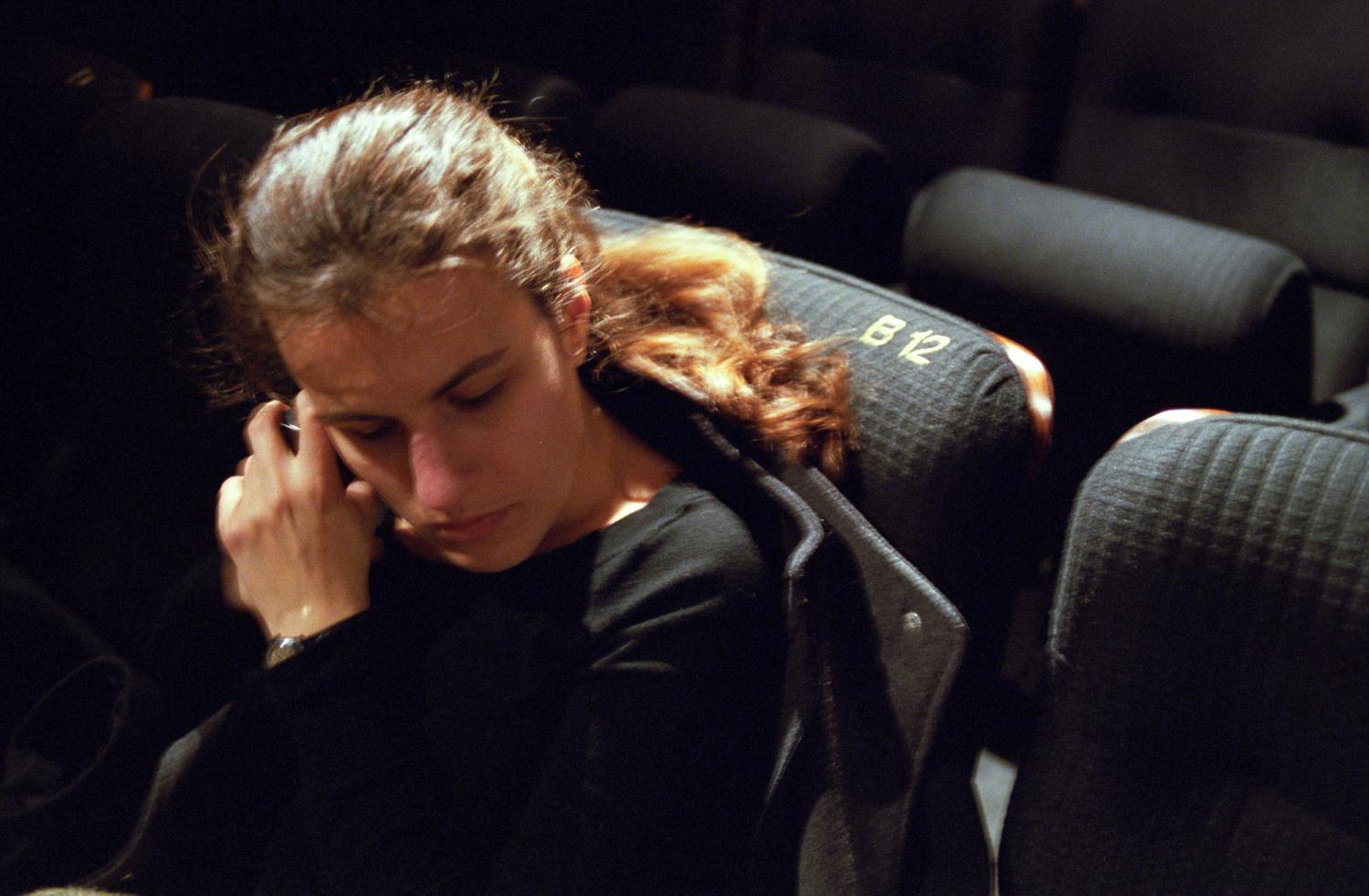 Céline dans un fauteuil de cinéma, la tête légèrement penchée vers son téléphone qu'elle tient à deux mains près de son oreille pour l'arrêter. Paris, mars 2006.
