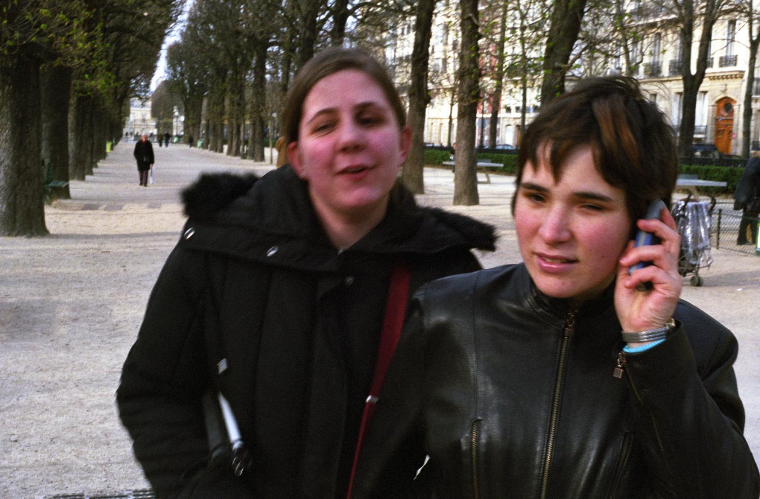Dans une allée du Petit Luxembourg, Audrey, le téléphone à l'oreille, devance et guide son amie Juliette qui a plié sa canne blanche sous son bras. Paris, avril 2006.