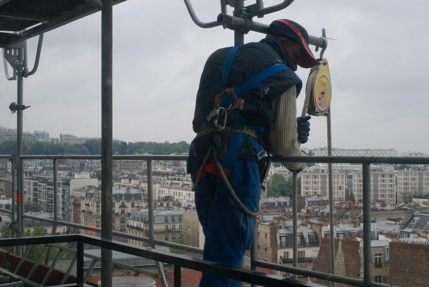 Un ouvrier en harnais sur l'échafaudage, devant une poulie, une corde à la main. Paris, mai 2010.