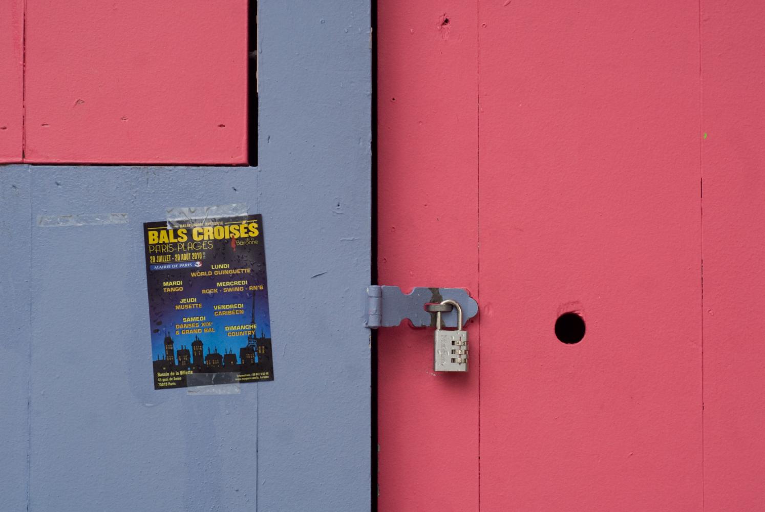 Détail d'une baraque peinte en mauve : les volets roses sont fermés, la porte rose cadenassée, et une affichette scotchée annonce le programme des bals de Paris Plage. Paris, août 2010.