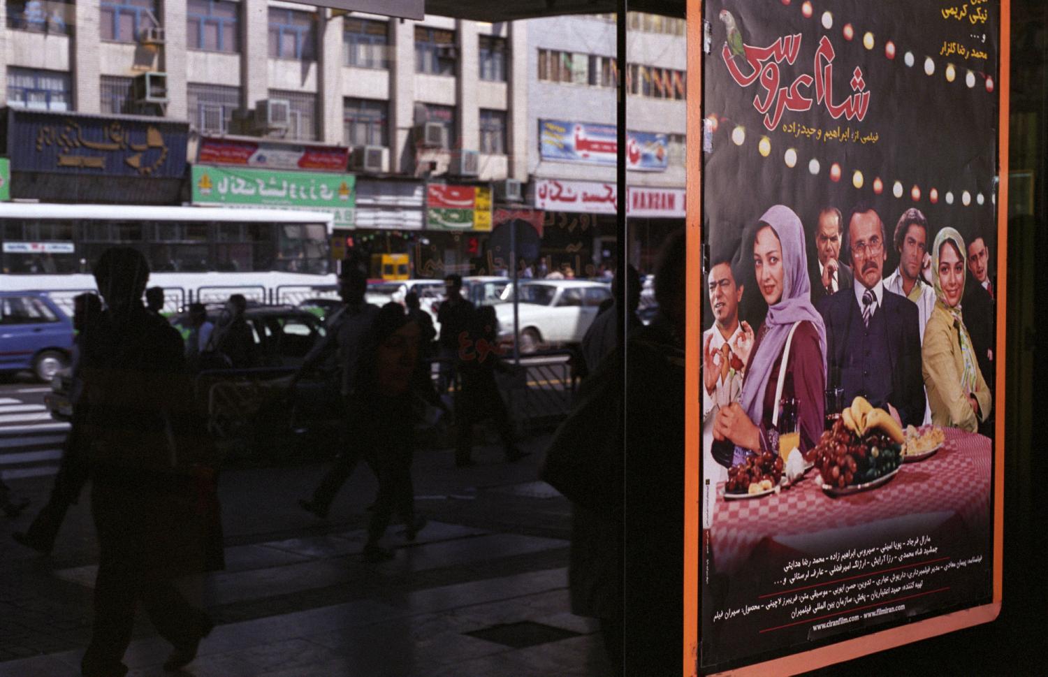 A la porte d’un cinéma d'Enqelab à Téhéran, l’affiche d’une comédie avec Niki Karimi, et le reflet des passants. Téhéran, Iran, septembre 2006.