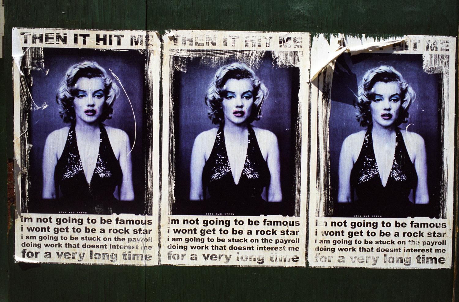 Une affiche collée trois fois sur une palissade vert sombre entoure une photo de Marylin Monroe de quelques mots désabusés. New York, juillet 2003.