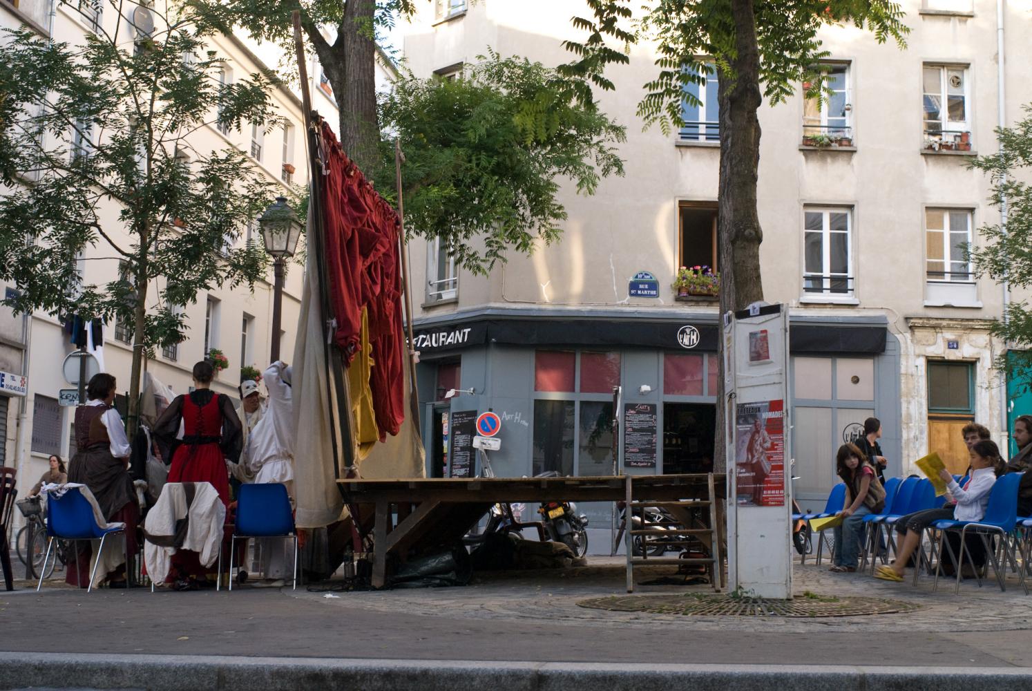 Posés place Sainte-Marthe, des chaises, une scène et des rideaux, derrière lesquels les comédiens se préparent. Paris, août 2010.