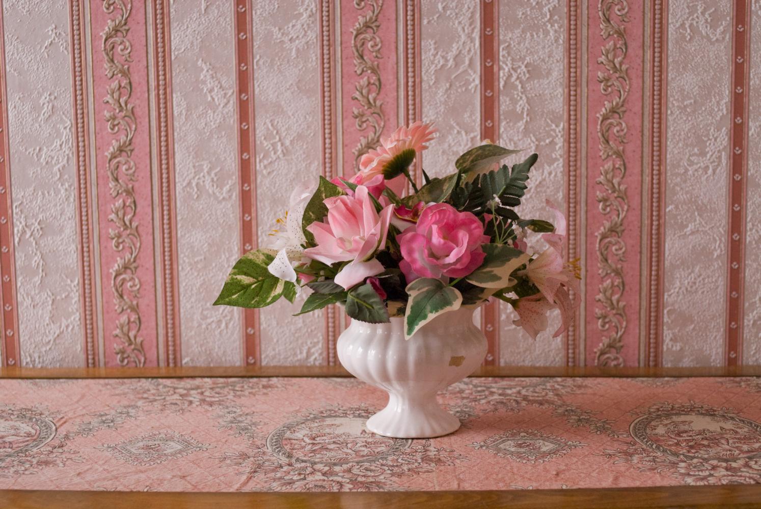 Bouquet de fleurs en plastique posé sur un meuble tapissé de rose, devant un papier peint de la même couleur. Nohant-en-Graçay, août 2009.