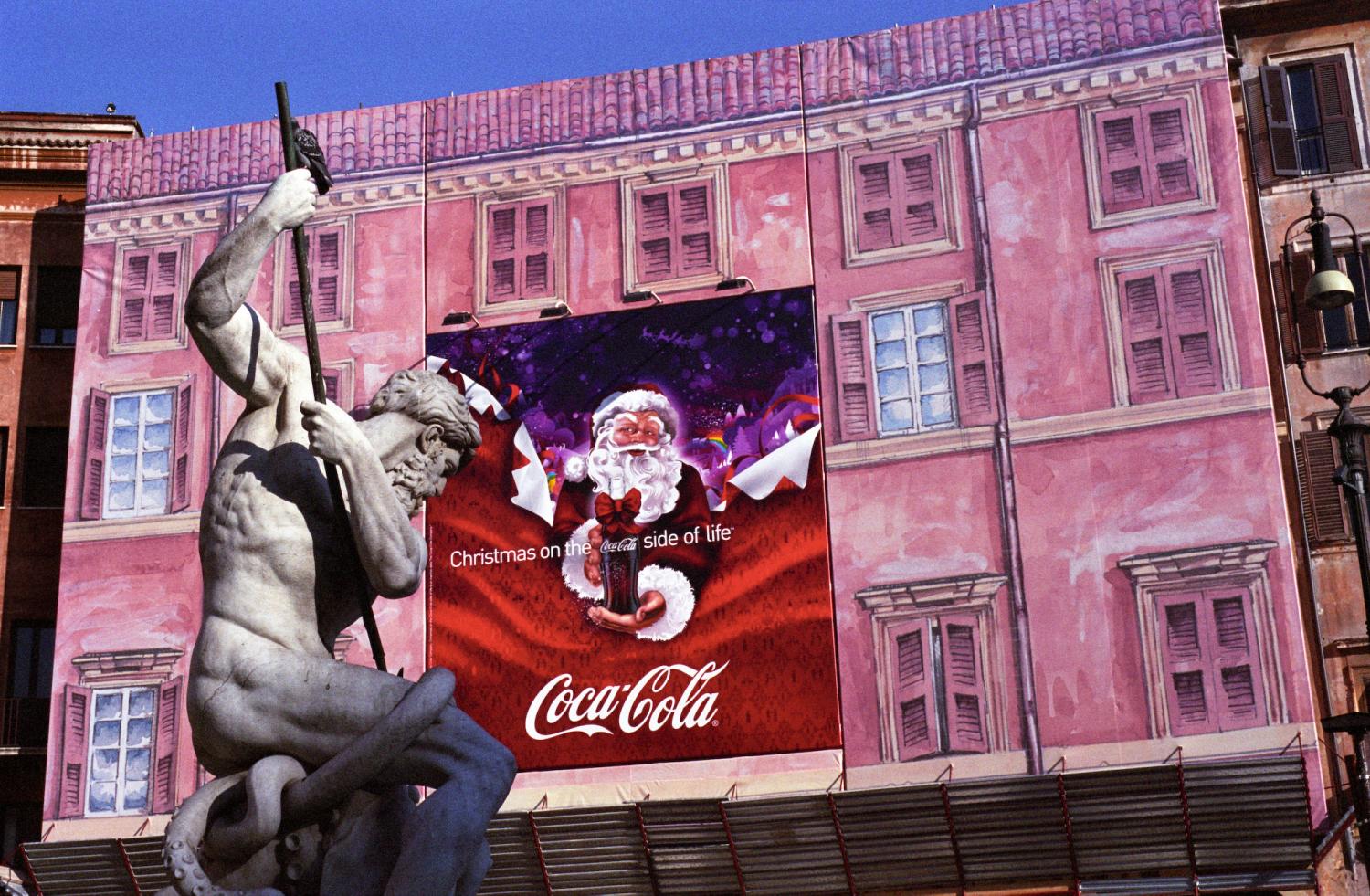 Piazza Navona, étalé sur la bâche en trompe-l'œil rose d'un échafaudage, le père Noël de Coca-Cola semble défier Neptune dans sa fontaine. Rome, décembre 2007.