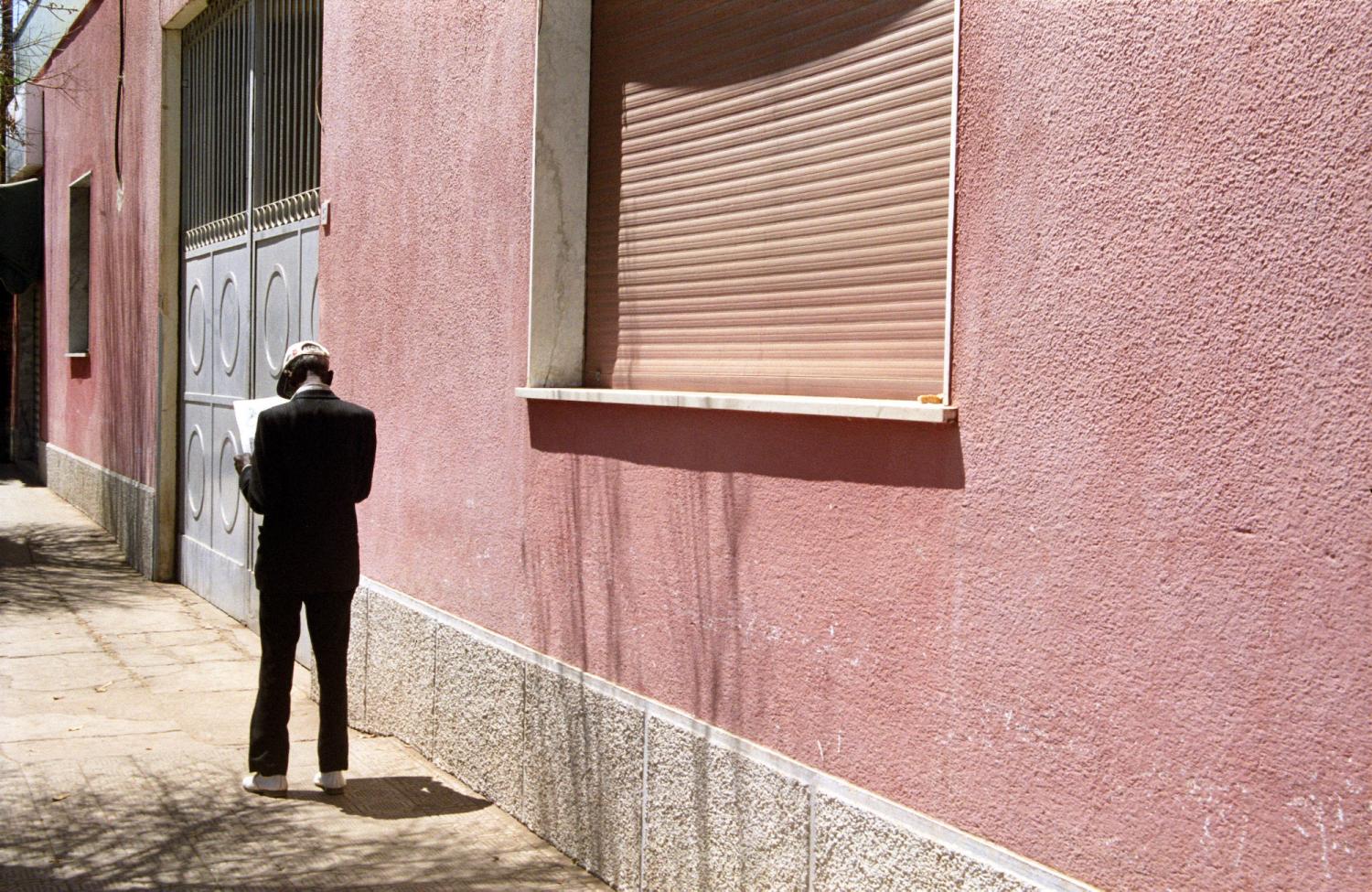 Un homme endimanché lit le journal en longeant un immeuble rose. Asmara, Erythrée, mars 2005.