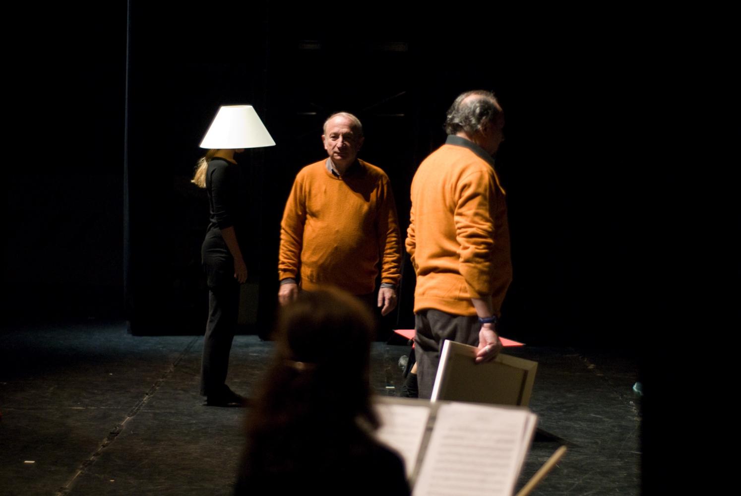 Derrière la silhouette d'une violoniste assise, les deux pères en pull-over orange et une choreute, en noir, avec un abat-jour sur la tête. Nanterre, octobre 2009.