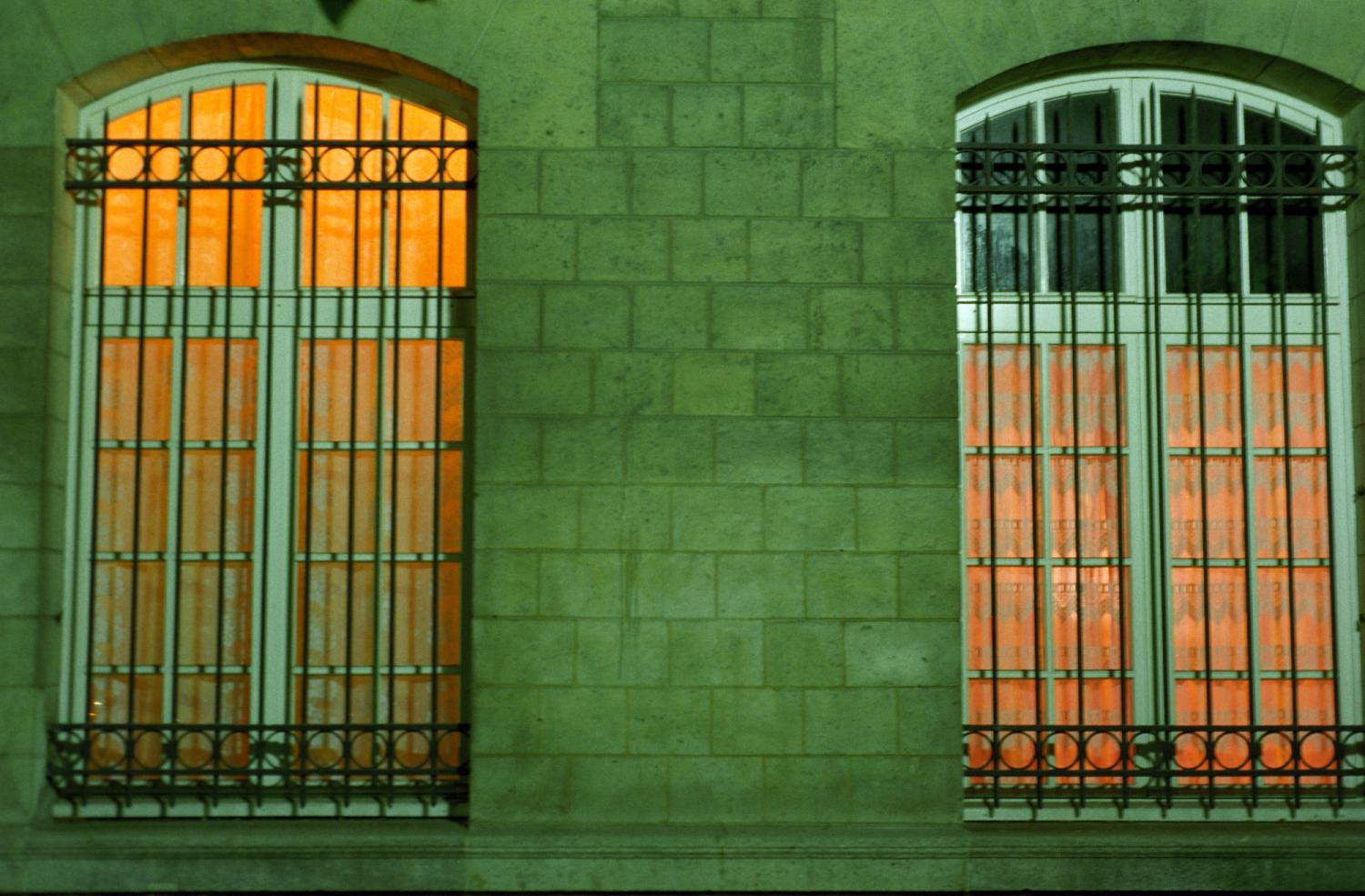 Vers Denfert-Rochereau, deux fenêtres illuminées jaune orangé d'un immeuble de pierre à la façade verdâtre. Paris, printemps 2006.